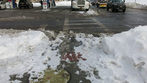 A slushy path through the snow bank connecting the crosswalk to the sidewalk.