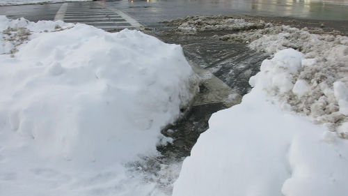 A street corner with a path shoveled through the snow pile.