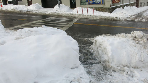 A street corner with a path shoveled through the snow pile.